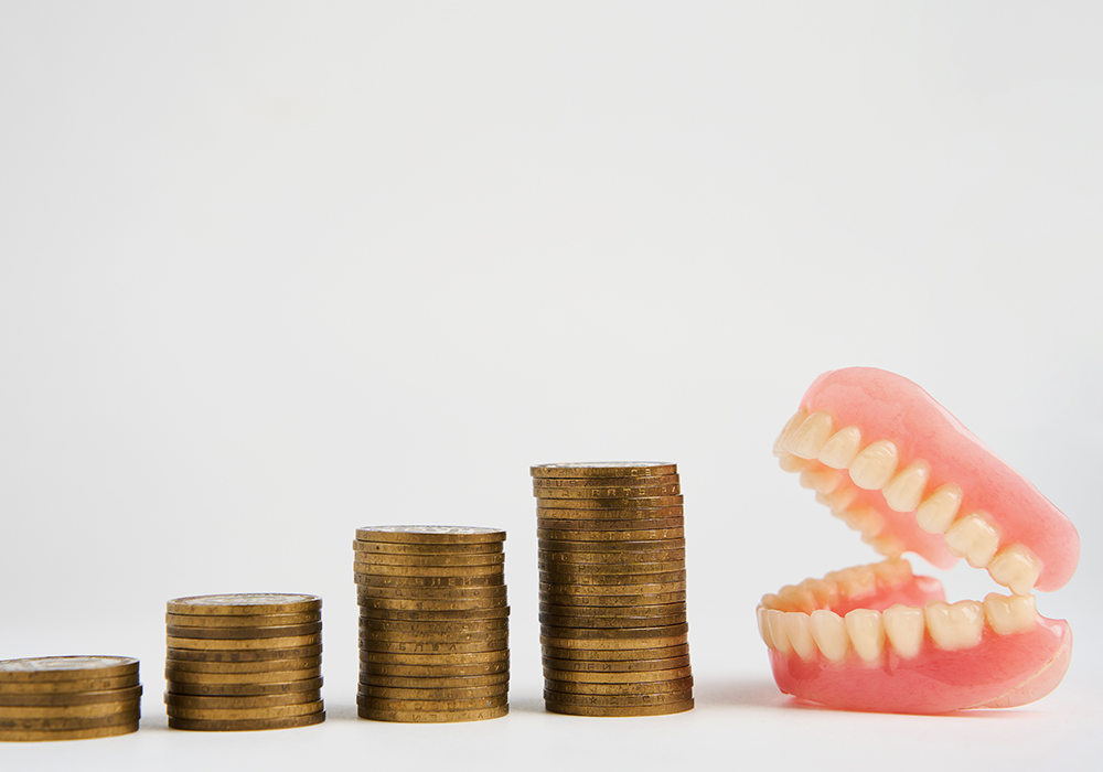 Dentures sitting next to separate stacks of coins