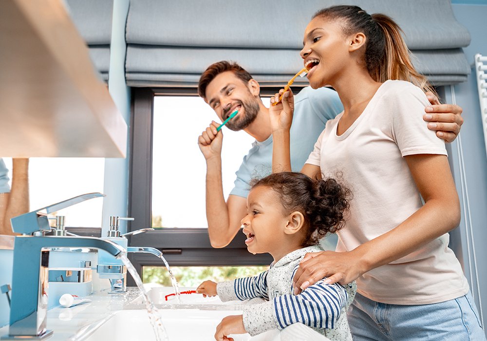 A small family of three brushing their teeth in the bathroom.