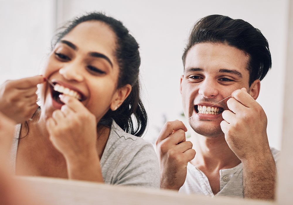 A couple flossing their teeth in the bathroom.