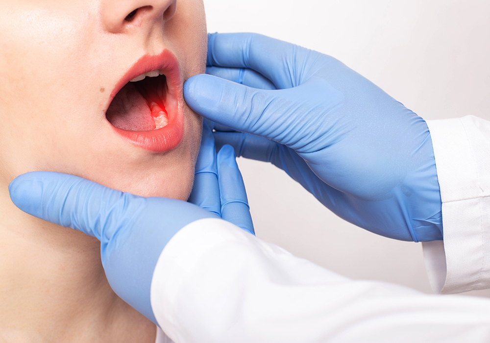 A man sitting in a dentist chair and touching his jaw while looking at the dentist
