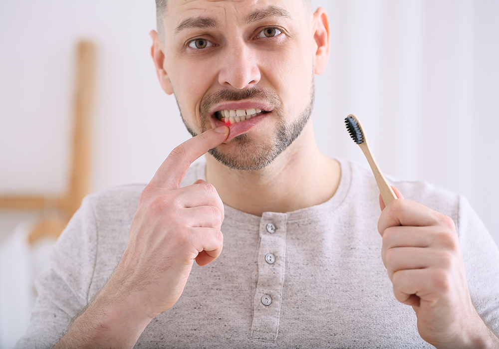 Male looking at himself in mirror while holding toothbrush with bleeding gums