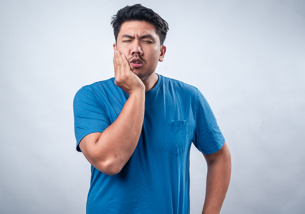 Man in blue shirt holding one side of his jaw