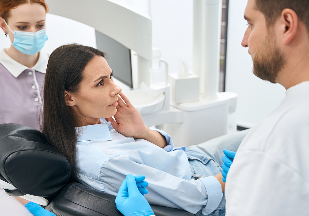 A woman is holding her swollen jaw while speaking with dentist