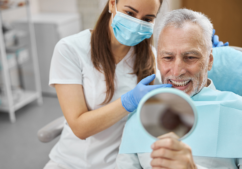 Man at denture fitting smiling as he admires his new smile in the mirror