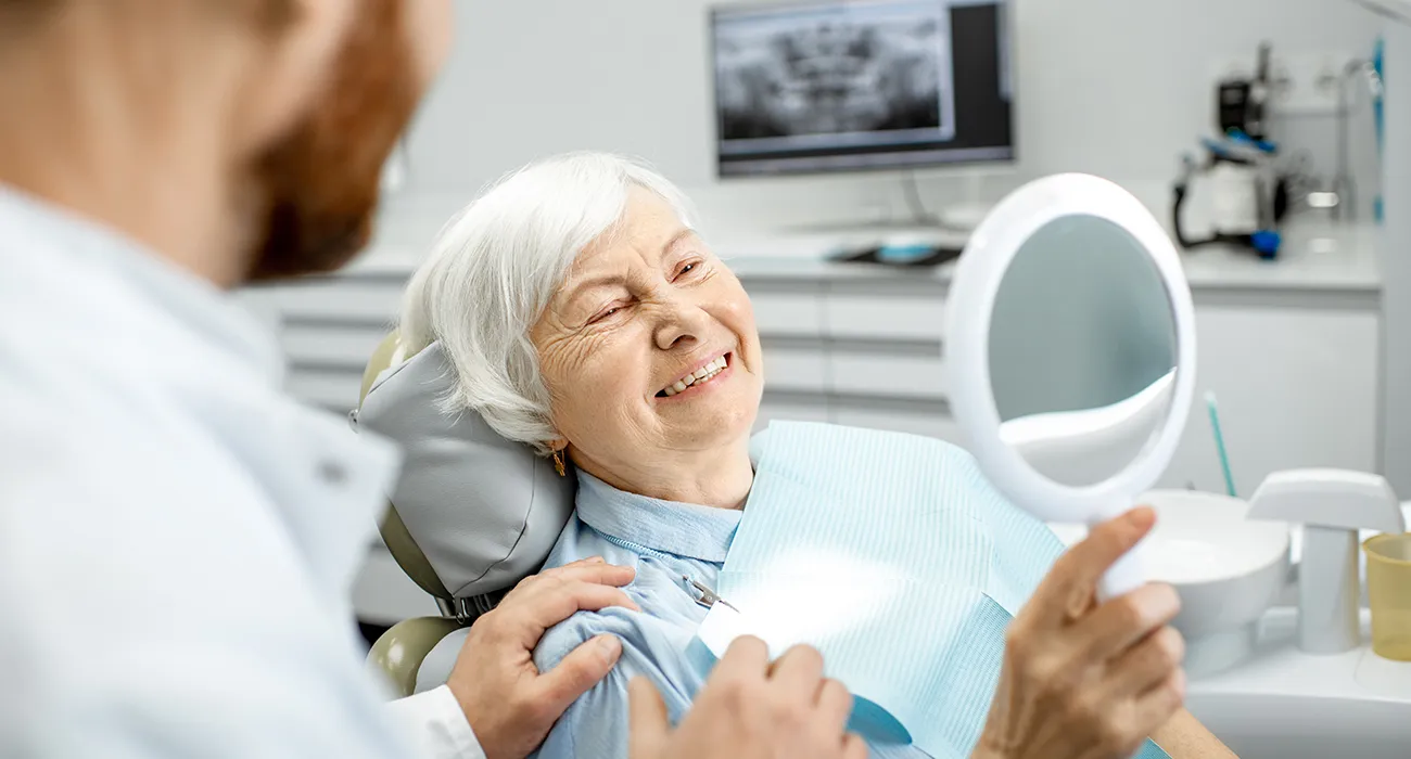 older woman looking at new dentures in mirror